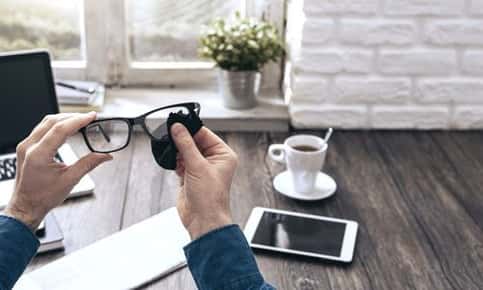 An image from the view of someone sitting at their desk while cleaning their classes with a soft cloth.