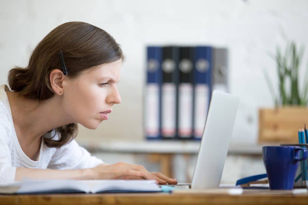 A woman experiencing eye strain squints and leans forward to stare at her laptop screen. 