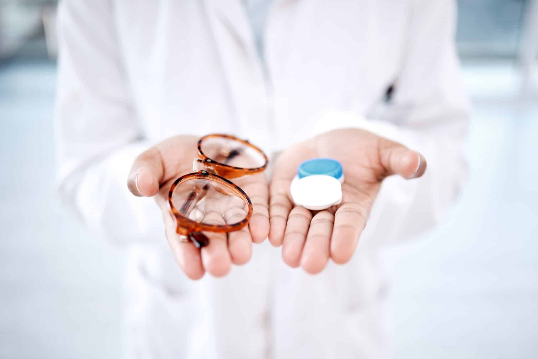 A close-up of an optometrist holding out their hands, one with glasses and the other with a case for contact lenses.