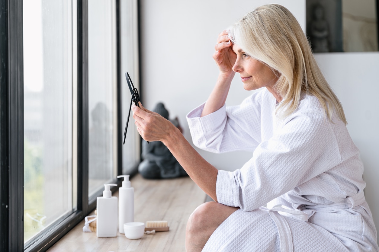 Middle-aged woman examining skin elasticity loss and fine lines in mirror as part of her collagen loss skincare routine.